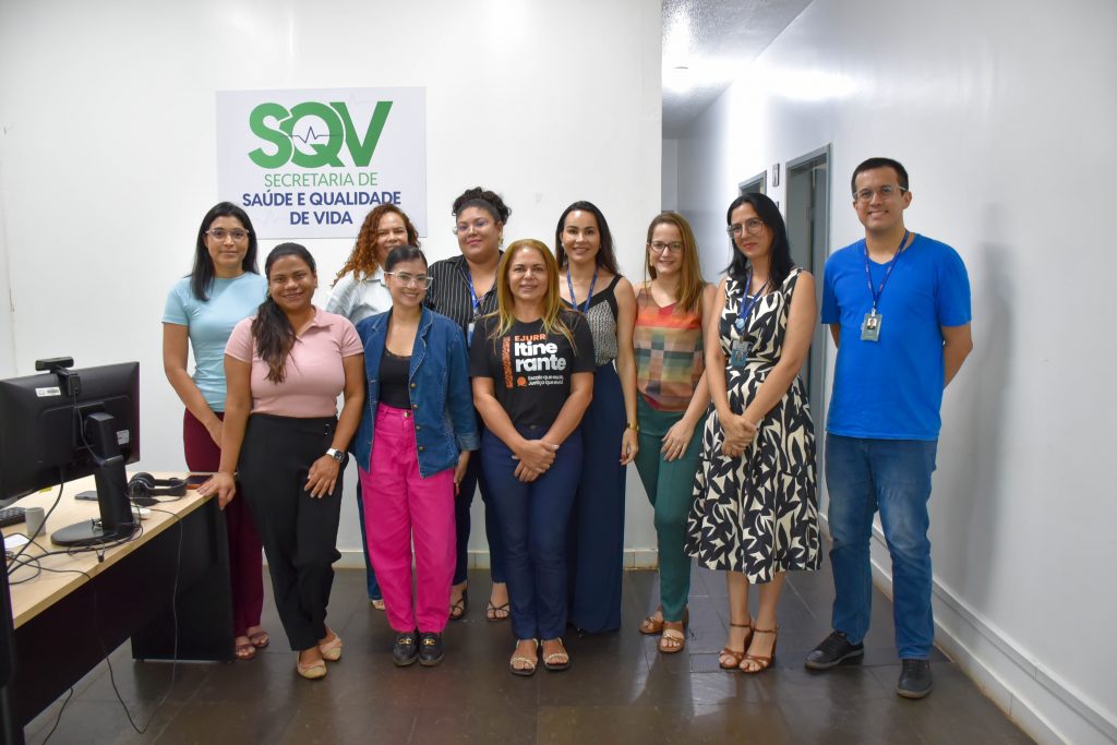 A imagem mostra um grupo de pessoas entre homens e mulheres de pé que sorriem em direção ao fotógrafo. No fundo, há uma placa escrita SQV.