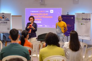 Um homem e uma muher estão de frente para o público. NO fundo, a projeção da Semana da Ibnovaçãoç CAD